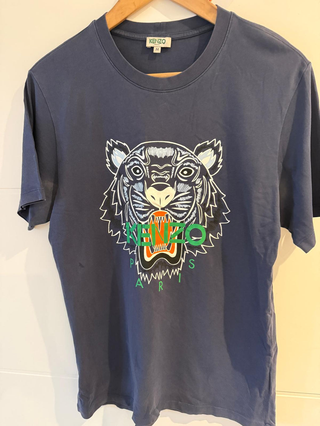 Navy blue t-shirt with a tiger logo and 'KENZO' branding on a wooden hanger.